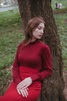 a girl in red rests leaning on a tree in the spring forest