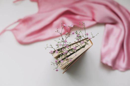 a book with flowers inside and pink silk fabric. Flat lay, top view, mock up