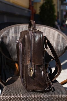 Brown leather backpack on the stylish chair. Outdoor photo