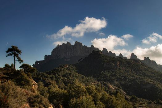 Montserrat mountain and a forest in front of it under a cloudy blue sky