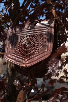 small burgundy women's leather bag with a carved pattern. street photo