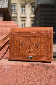 small orange women's leather bag with a carved pattern. street photo