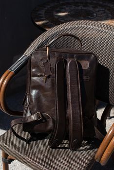 Brown leather backpack on the stylish chair. Outdoor photo