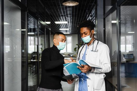 Discussion and consultation between black doctor and patient in medical clinic. African surgeon treats Asian handsome man