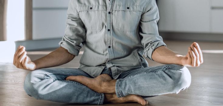 handsome young man sitting in Lotus position on kitchen floor.