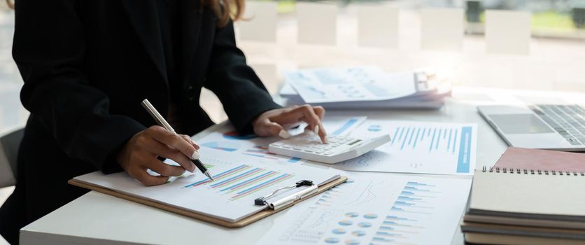 Close up of businessman or accountant hand holding pen working on calculator and laptop computer to calculate business data during make note at notepad, accountancy document at office.