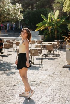 Girl tourist walking through ancient narrow street on a beautiful summer day in MEDITERRANEAN MEDIEVAL CITY , OLD TOWN bUDVA, MONTENEGRO. Young beautiful cheerful woman walking on old street at tropical town. Pretty girl looking at you and smiling