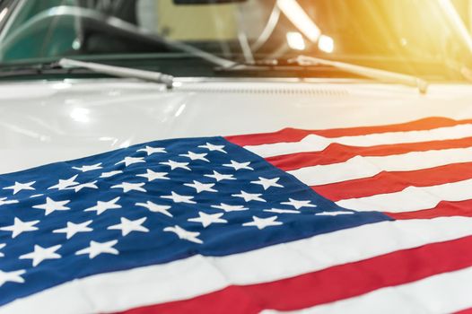 USA flag on the hood of a white car with sunlight