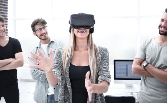 young excited woman testing VR glasses or goggles sitting in the office room with two colleagues, teleconference