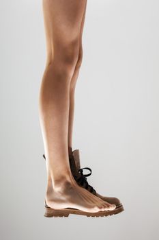 Sexy female legs wearing one waterpfoor boot against gray background.