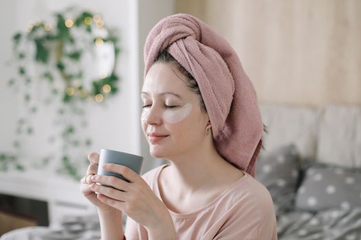 Young woman with eyes patches and towel on head at home. Morning habits and home beauty routine