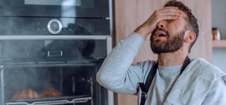 surprised man standing near the oven with burnt croissants. photo with copy space