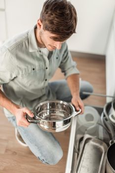 happy young man looking at clean dishes in dishwasher