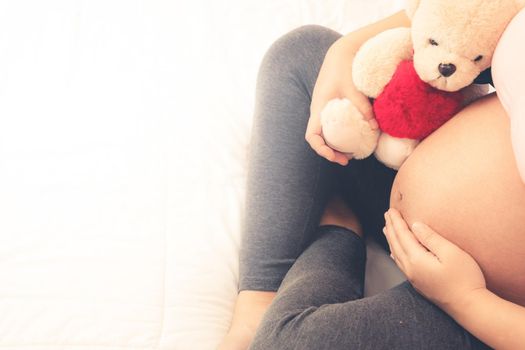 Pregnant woman feeling happy at home while taking care of her child. The young expecting mother holding baby in pregnant belly. Maternity prenatal care and woman pregnancy concept.