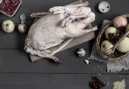 On the kitchen table there is a duck carcass next to the products for its further preparation: apples and berries for stuffing, spices and vegetables