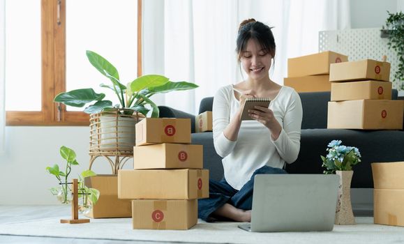 Startup small business owner working with computer at workplace. Freelance woman seller check product order. Packing goods for delivery to customer. Online selling. E-commerce.