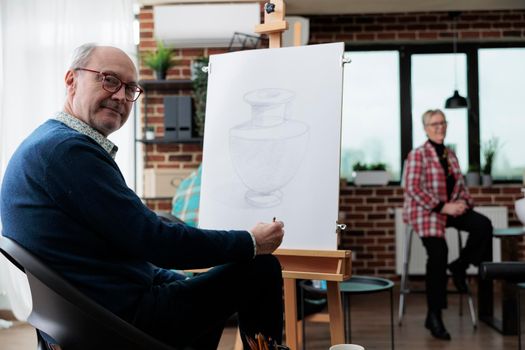 Portrait of class senior student standing in front on painting canvas drawing artistic vase using sketching technique during art lesson in creativity studio. Elderly painter havnig creative hobby