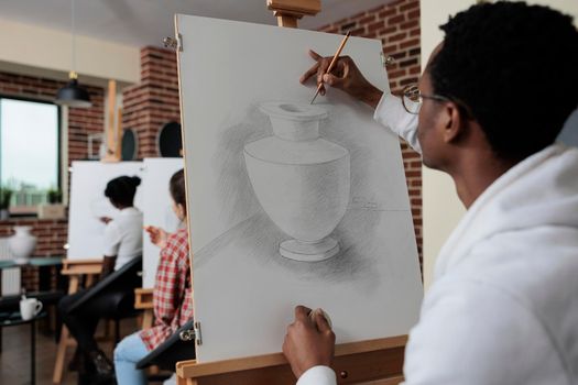 African american student attending art lesson working at creative artwork drawing vase model using graphic pencil in creativity studio. Multiethnic team sketching draw. Creative concept