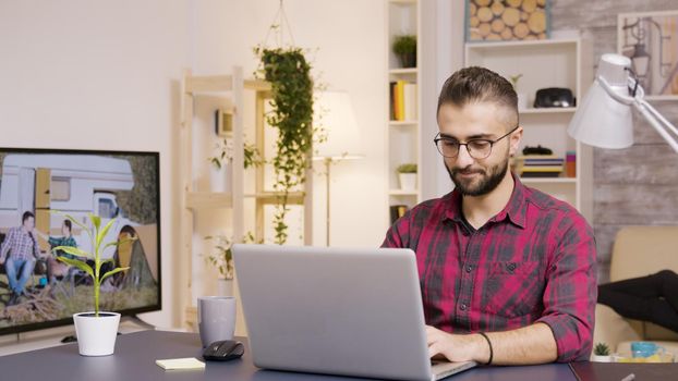 Freelancer taking a sip of coffee while working on laptop in living room. Girlfriend in the background watches TV.