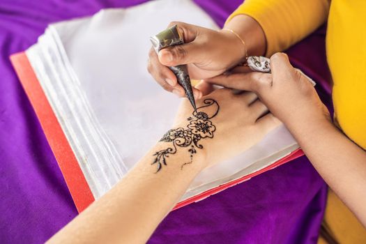 Woman is drawing on hand. Draw on the hand Indian mehendi picture.