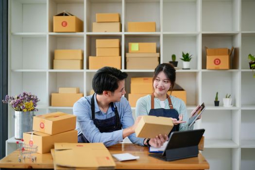 startup small business owner working with tablet at workplace. freelance man and woman seller check product order, packing goods for delivery to customer. Online selling, e-commerce, shipping concept.