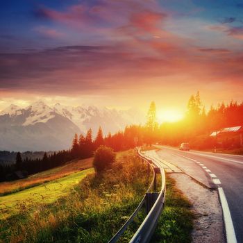 Fantastic sunset that leads into the mountains. Asphalt road with white markings. Beautiful summer landscape. Soft filtered effect. Europe