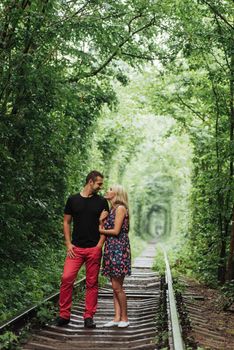 Loving couple in a tunnel of green trees on railroad.