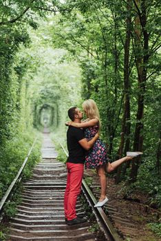 Loving couple in a tunnel of green trees on railroad.