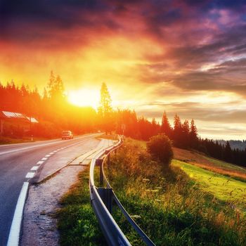 Fantastic sunset that leads into the mountains. Asphalt road with white markings. Beautiful summer landscape. Soft filtered effect. Europe