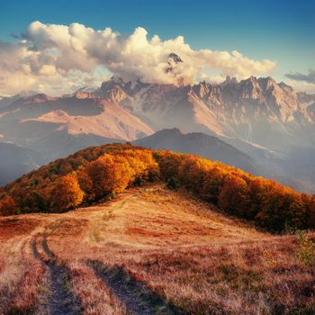 Autumn road in the mountains. Fantastic cumulus clouds, dramatic skies. Dramatic scene. Sunset. Europe