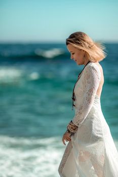 Middle aged woman looks good with blond hair, boho style in white long dress on the beach decorations on her neck and arms