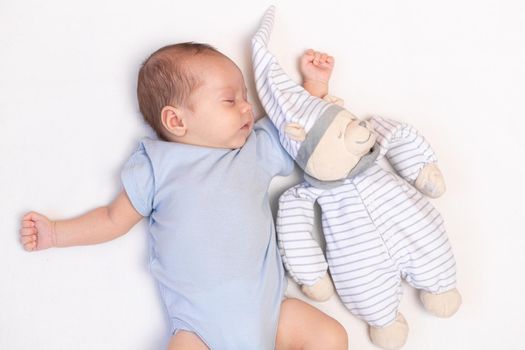 The baby is lying in a crib with a teddy bear . The baby is 0-3 months old. A calm sleeping baby. Healthy baby sleep. An article about toys for kids. A soft toy. Copy Space