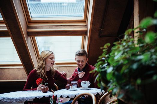 Beautiful young man and woman are celebrating Valentine day at restaurant. The man is giving a rose to his girlfriend