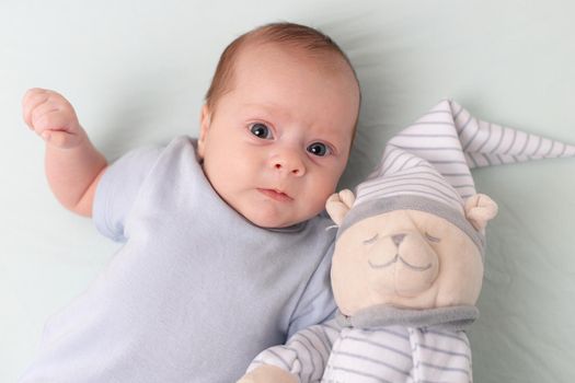 The baby is lying in a crib with a teddy bear . The baby is 0-3 months old. Calm kid. An article about toys for kids. A soft toy. Copy Space