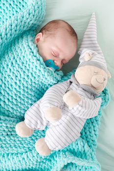 The baby is lying in a crib with a teddy bear . The baby is 0-3 months old. A calm sleeping baby. Healthy baby sleep. An article about toys for kids. A soft toy. Copy Space