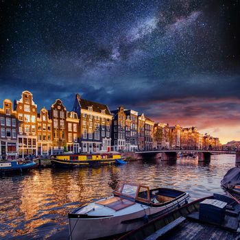 Beautiful night in Amsterdam. Night illumination of buildings and boats near the water in the canal.