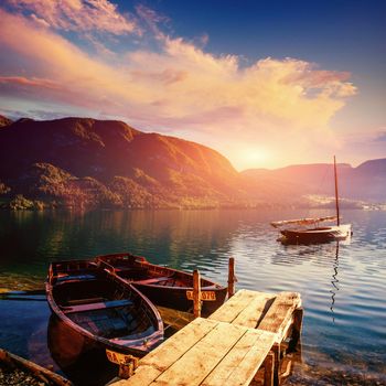 Fantastic sunset on a lake between mountains and wood masonry leading to the boats.