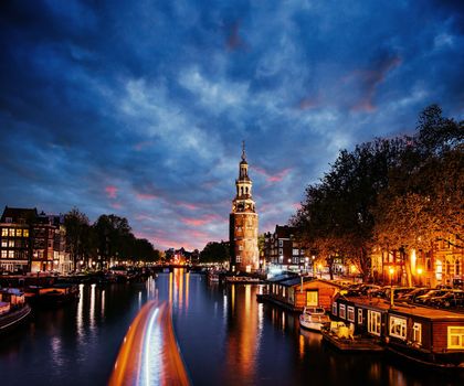 Beautiful in Amsterdam. Night illumination of buildings and boats near the water in the canal.
