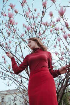 a veth-haired girl in red against the background of a magnolia tree. the concept of unity with nature