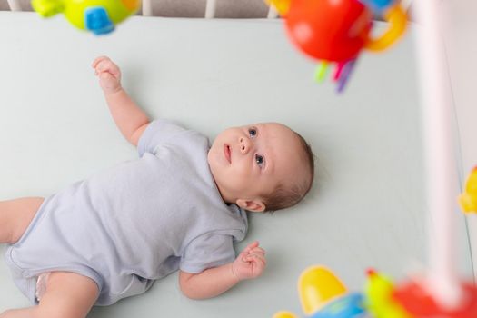 The baby looks at the mobile lying in the crib . Mobile to the crib. An article about kids' leisure. Mom's hands are free. An article about choosing a mobile in the crib. The baby is 0-3 months old. An infant