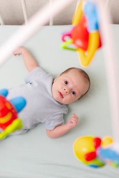 The baby looks at the mobile lying in the crib . Mobile to the crib. An article about kids' leisure. Mom's hands are free. An article about choosing a mobile in the crib. The baby is 0-3 months old. An infant