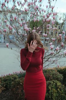 a veth-haired girl in red against the background of a magnolia tree. the concept of unity with nature