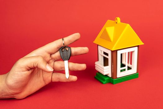 A woman's hand holding the key to the house, and a model of the house. mortgage. Real estate agent, apartment keys. buying or renting a house.