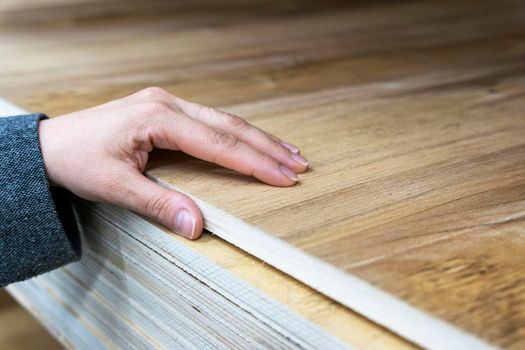 the buyer's hand selects a thick sheet of laminated wooden plywood in a construction store. checking the quality of the wooden sheet . Sale of wooden building materials