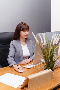 A brunette woman at a computer in the workplace. Business concept.