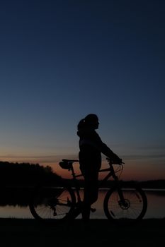 Silhouette of woman with a bike at sunset. Active outdoors lifestyle for healthy concept.