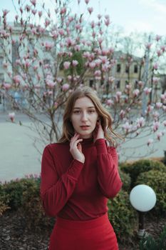a veth-haired girl in red against the background of a magnolia tree. the concept of unity with nature