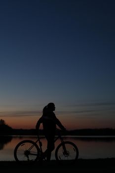 Silhouette of woman with a bike at sunset. Active outdoors lifestyle for healthy concept.
