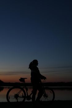 Silhouette of woman with a bike at sunset. Active outdoors lifestyle for healthy concept.