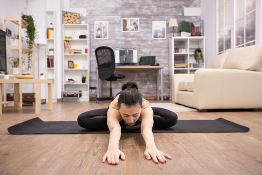 Young woman practicing peaceful medittating on mat sitting on lotus pose stretching forward.